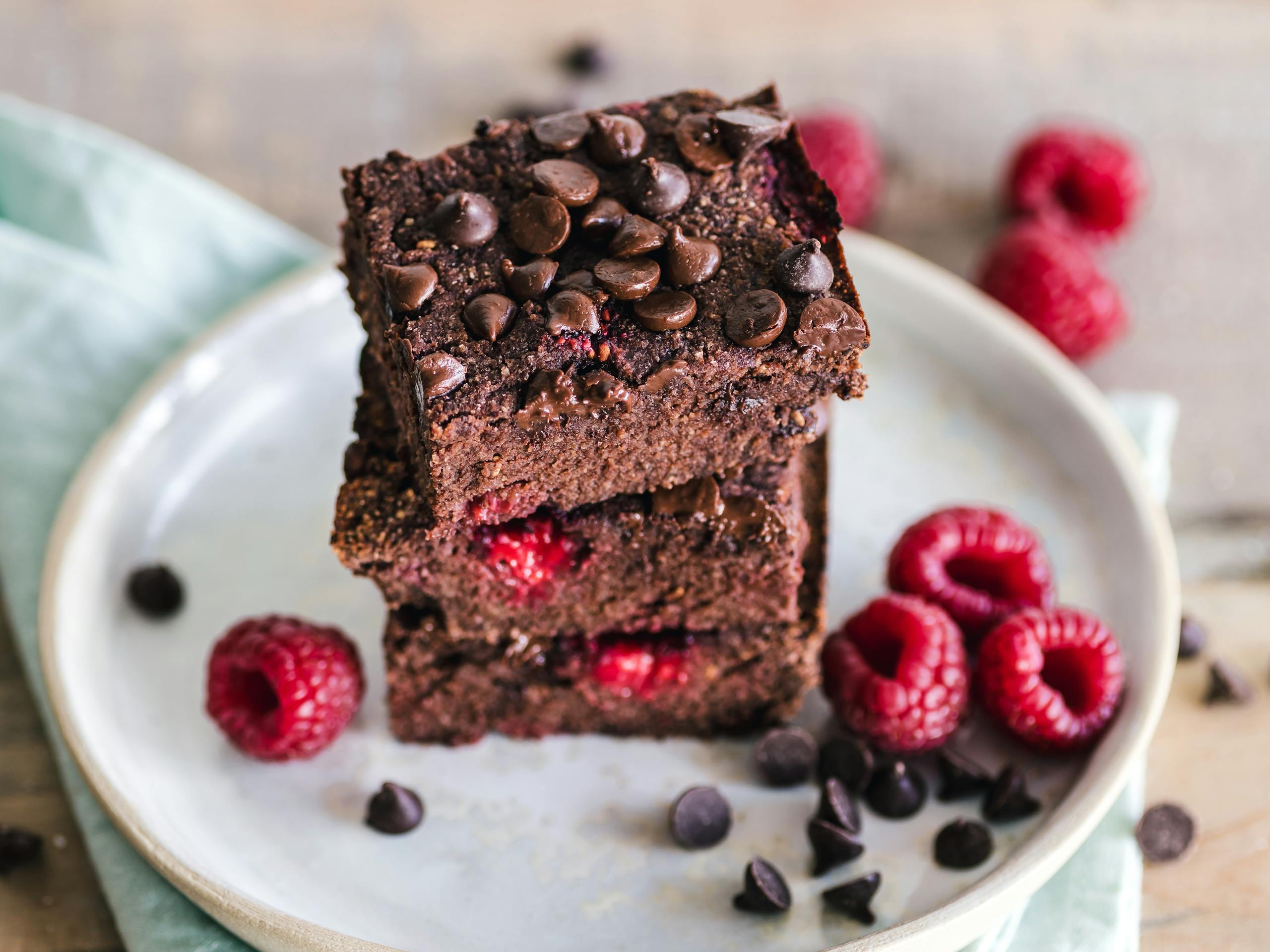 Close-up of deliciously indulgent chocolate raspberry brownies stacked on a ceramic plate with fresh raspberries.