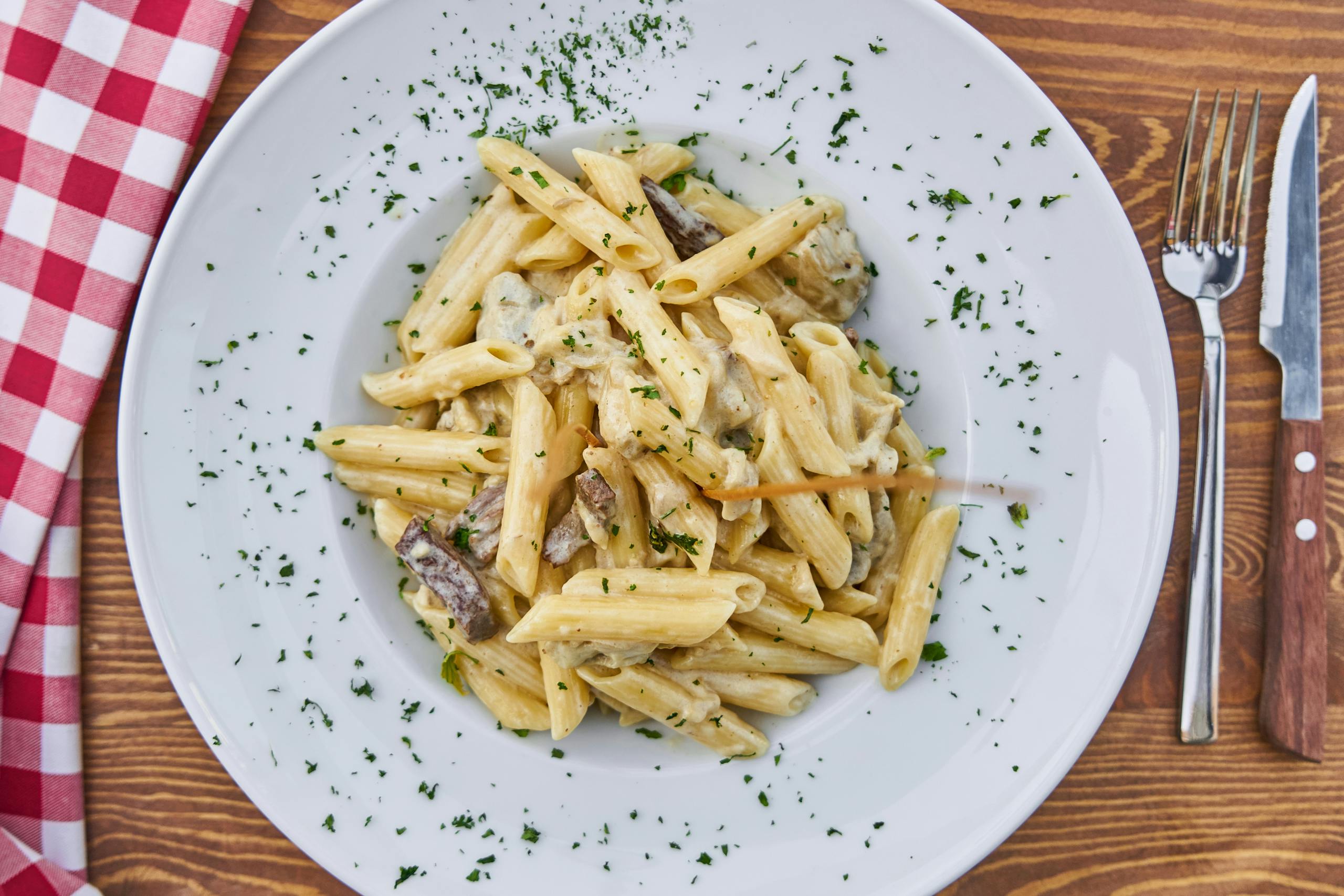 Delicious creamy penne pasta with mushrooms and parsley on a rustic table setting.