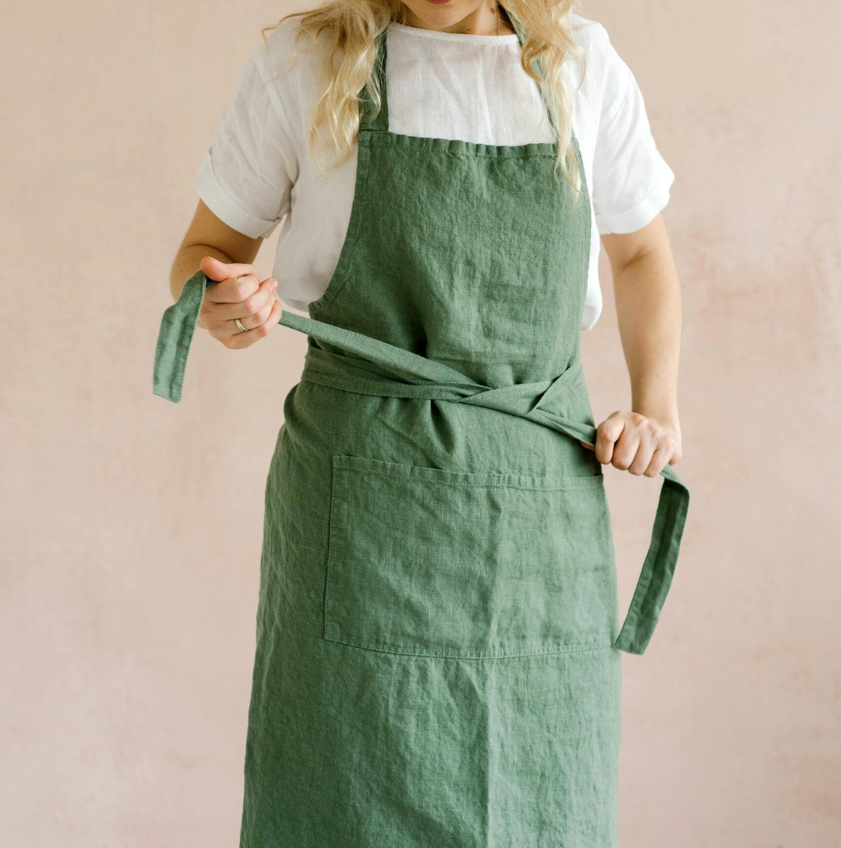 A woman in a green apron adjusts it, standing against a neutral background indoors.