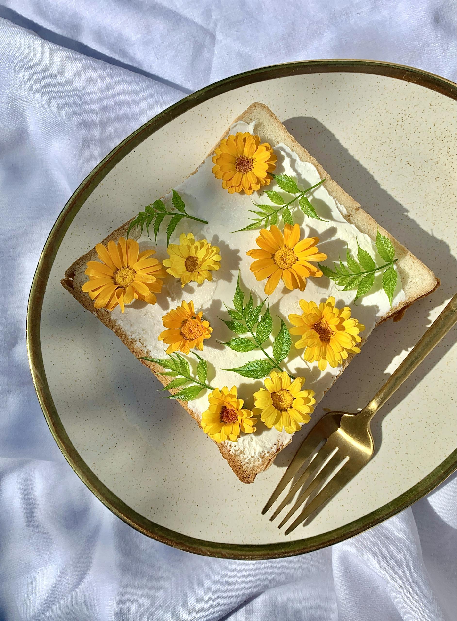 Artistic toast with edible flowers and leaves on a plate with a golden fork.