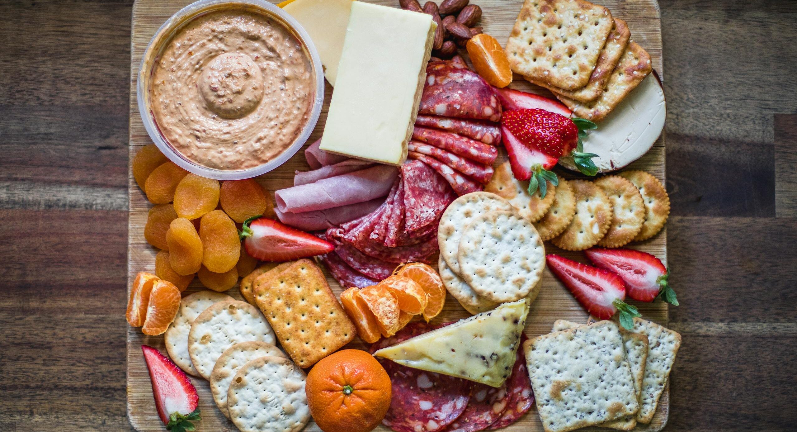 Delicious assortment of cheeses, cured meats, and fruits on a wooden platter.