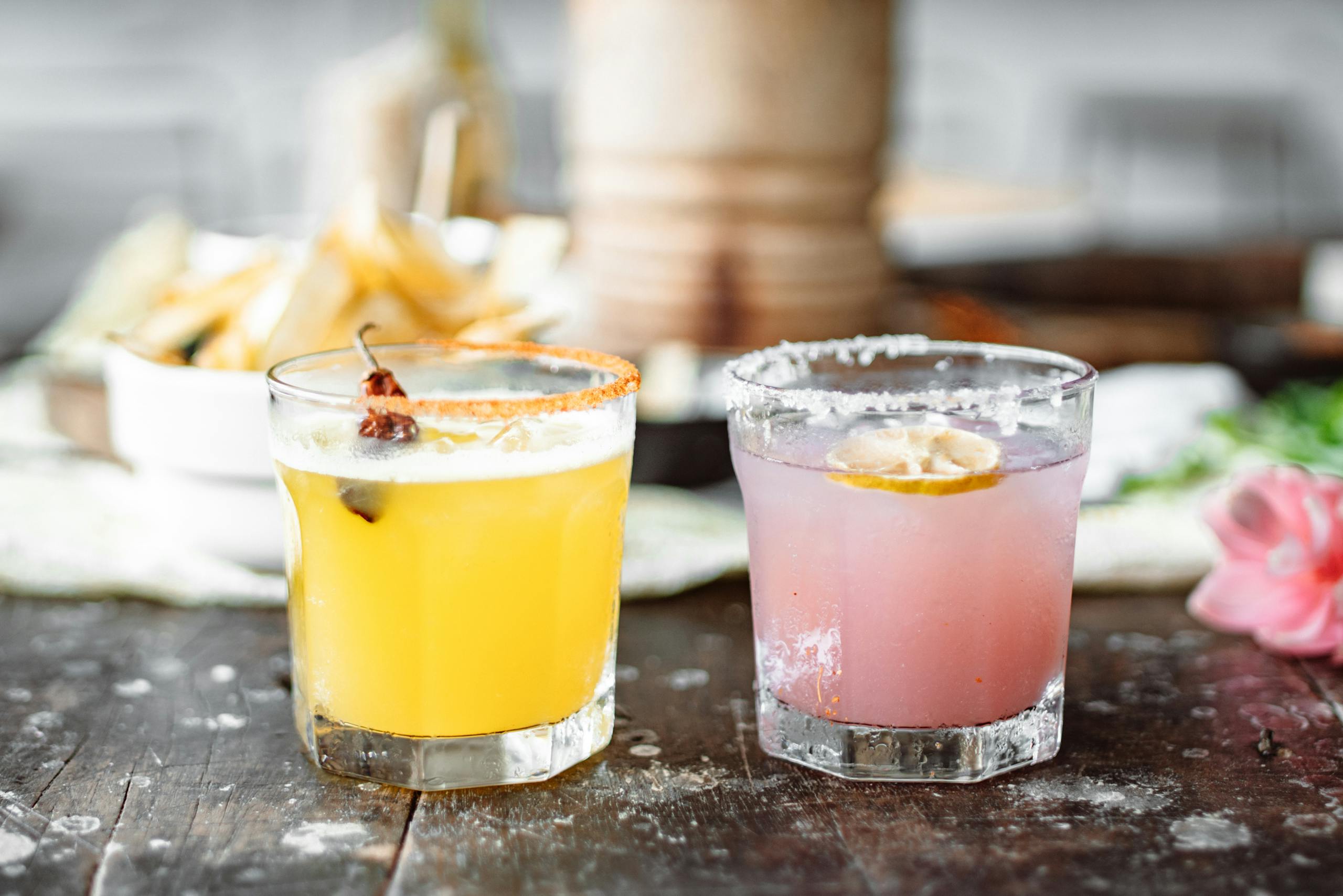 Two colorful cocktails with citrus garnish on a rustic wooden table, perfect for summer refreshment.