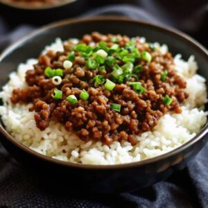 Cooked ground beef on a bed of rice in a bowl and chopped spring onion garnish.