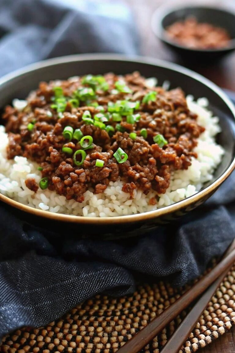 Cooked ground beef on a bed of rice in a bowl and chopped spring onion garnish.