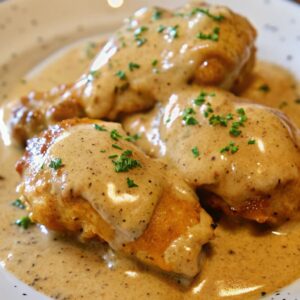 Southern smothered chicken in gravy with a sprinkle of herb garnish.