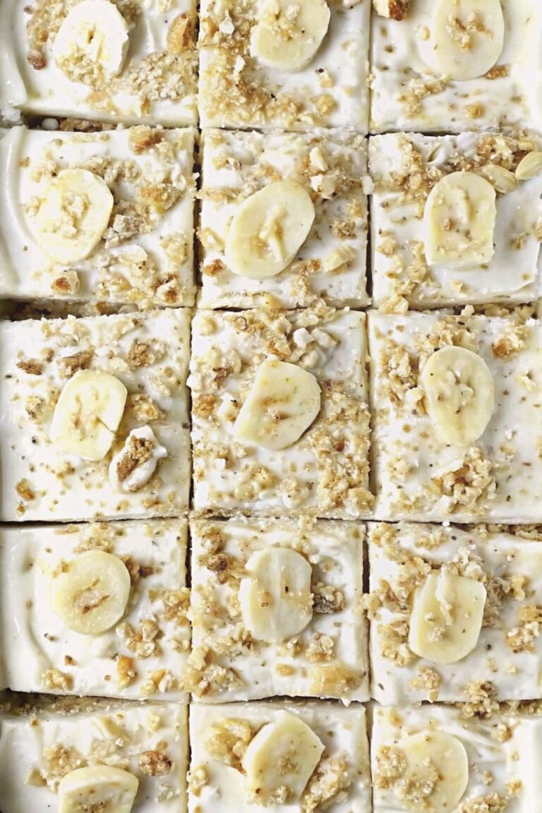 Square slices of banana bread cake with frosting and walnut garnish with banana slices.