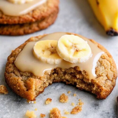 Banana bread cookies with glaze icing and banana slice on top with a bite taken.