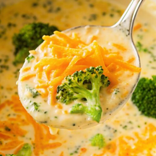 A metal spoon with a spoonful of broccoli and cheese soup from a pan.