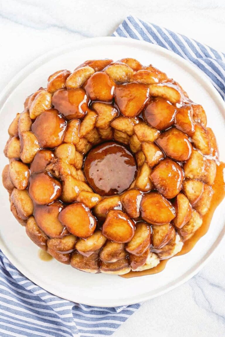 Monkey bread covered in a sweet gooey sauce served on a plate on a white marble countertop with a blue striped tea towel.